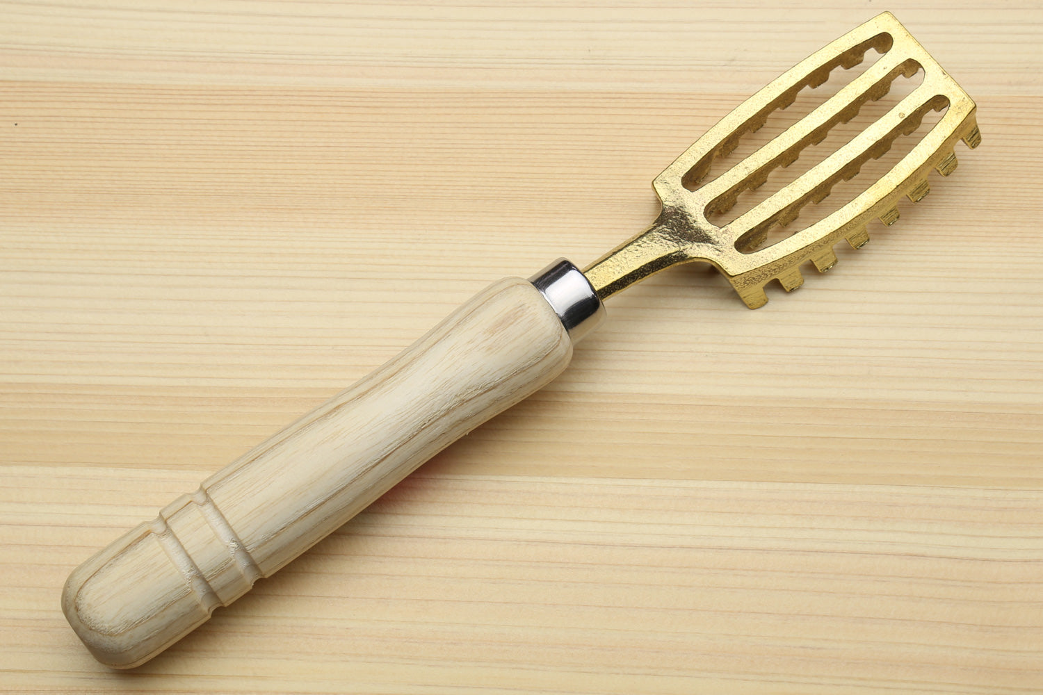 Fish scaler tool with light wood handle and gold metal head with raised ridges
