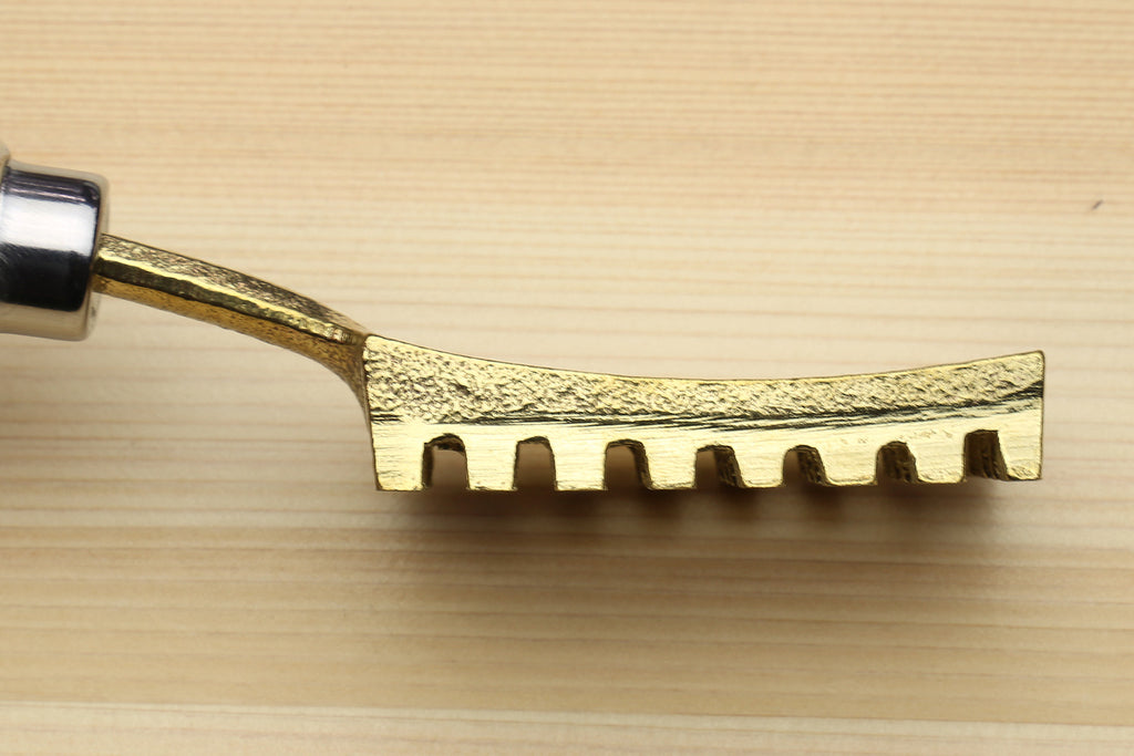 Gold metal fish scaler head with serrated teeth, shown in close-up
