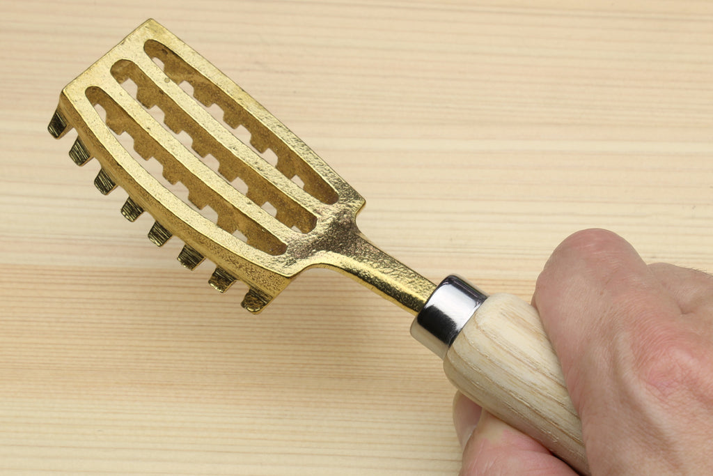 Fish scaler tool held by hand, light wood handle with gold ridged head
