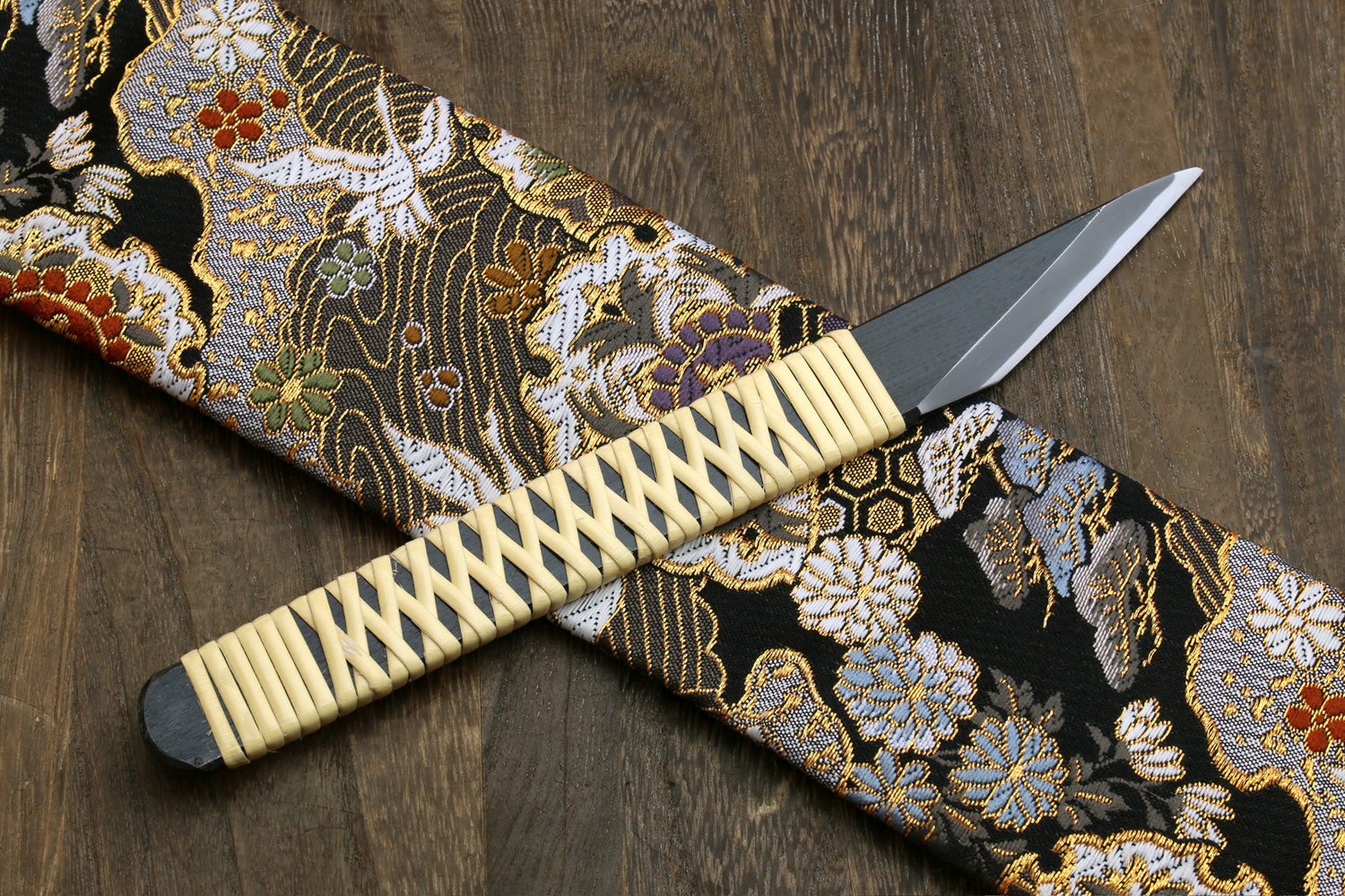 Kiridashi utility knife with beige braided handle and silver blade over patterned cloth