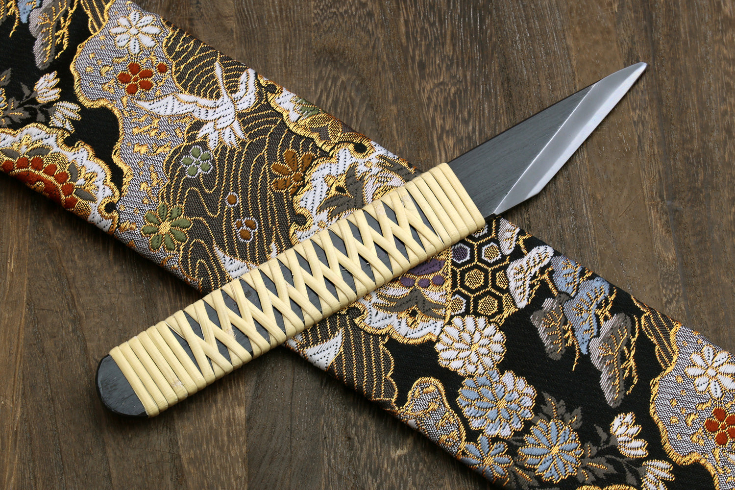 Kiridashi utility knife with beige braided handle and silver blade beside patterned fabric