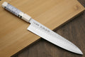 Gyuto chef knife on board with hammered stainless blade and white handle, ivory bolster