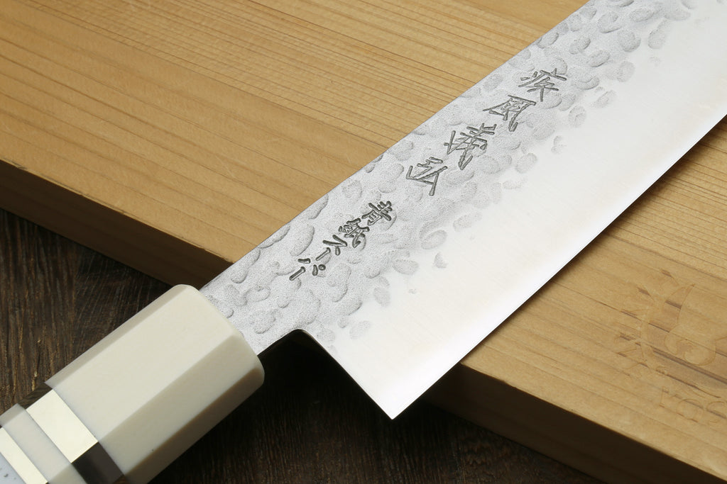 Chef's gyuto knife showing carved white handle and engraved hammered blade