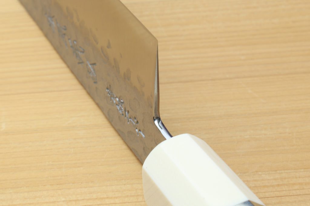 Chef's gyuto knife with white handle and hammered stainless blade edge detail