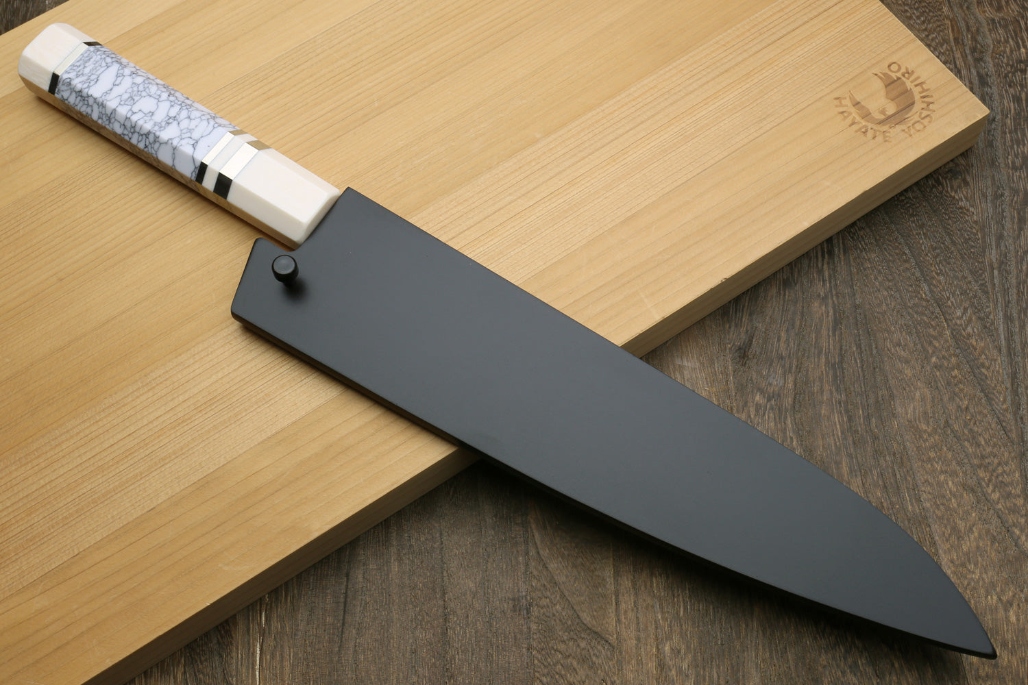Chef's gyuto knife with dark bolster, gray crackle handle scales, and broad blade