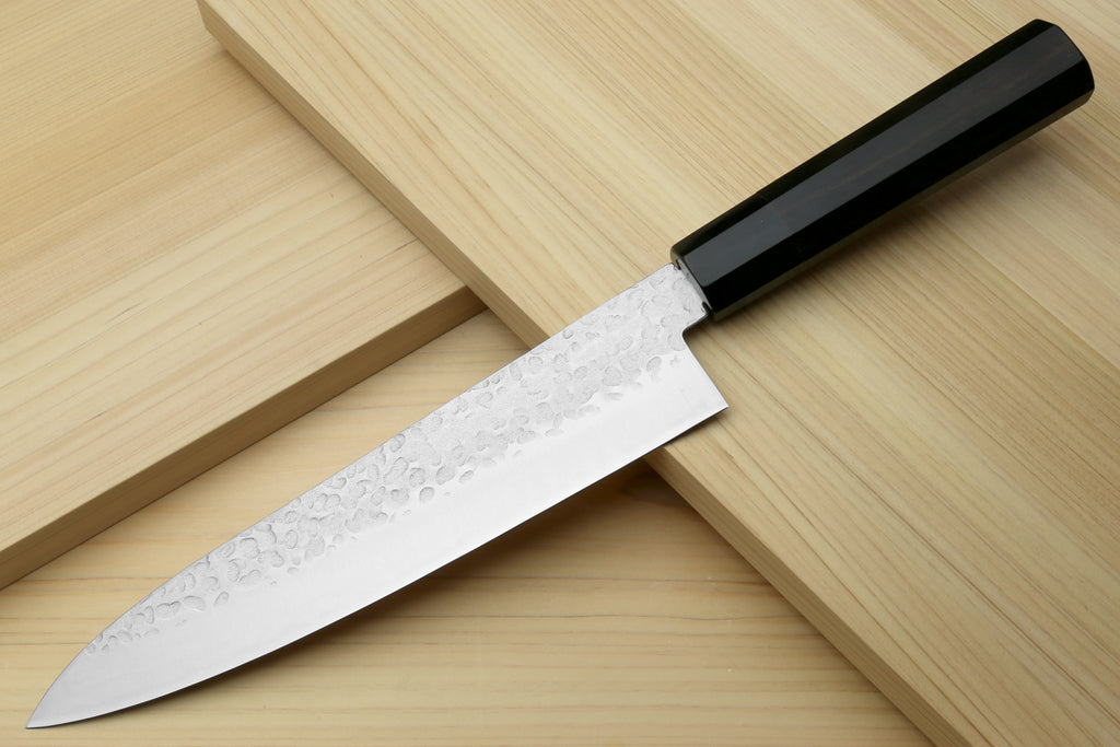 Hammered stainless gyuto chef's knife with ebony handle, angled on wood