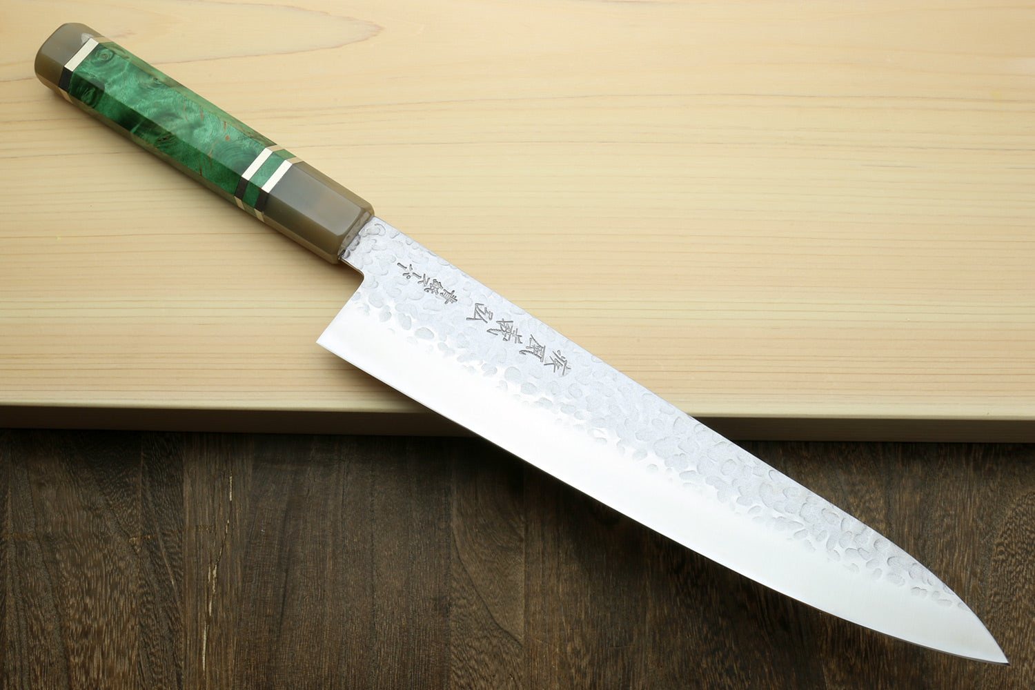 Gyuto chef knife with hammered stainless blade and green stabilised handle on board
