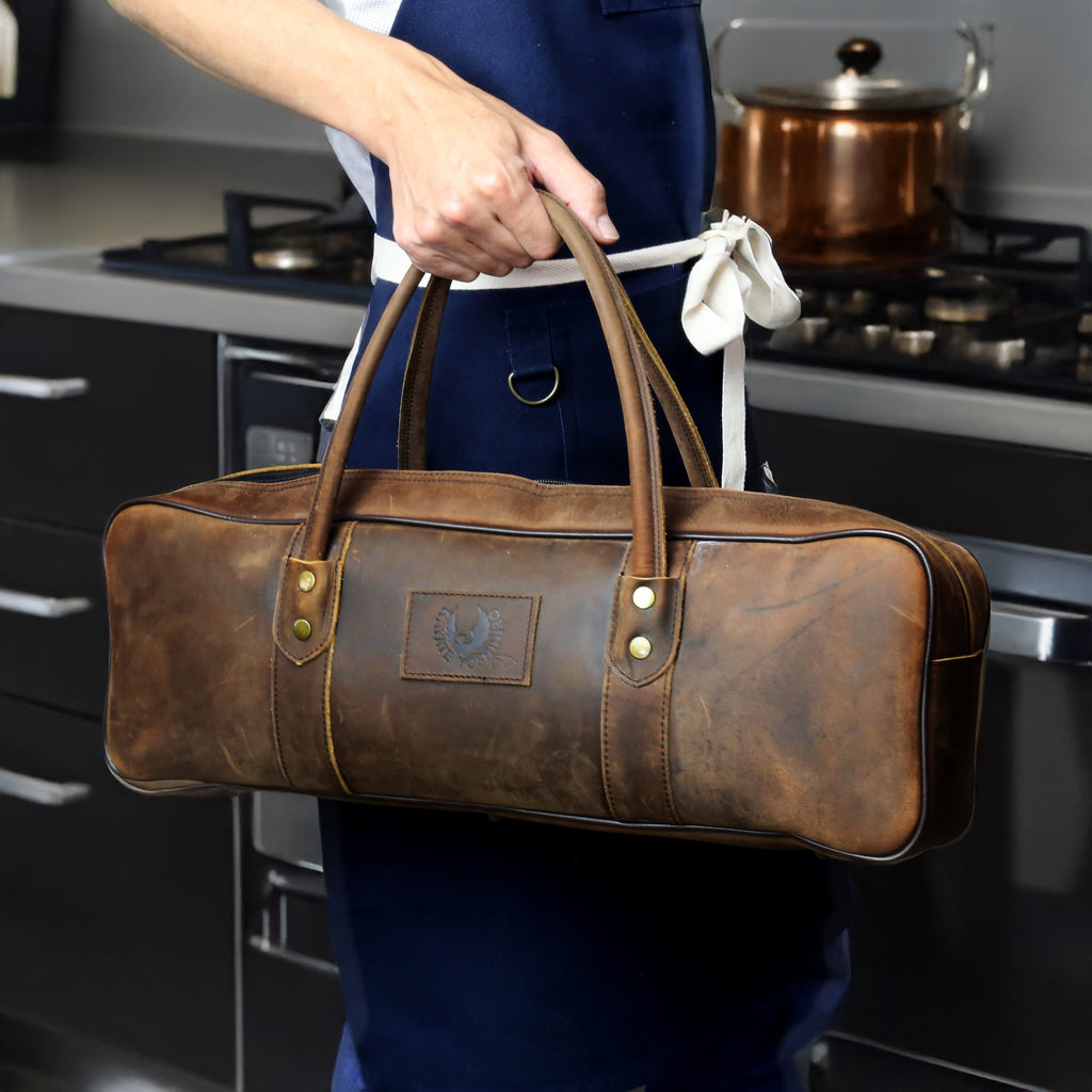 Brown natural leather knife bag carried in kitchen with front emblem and top handles