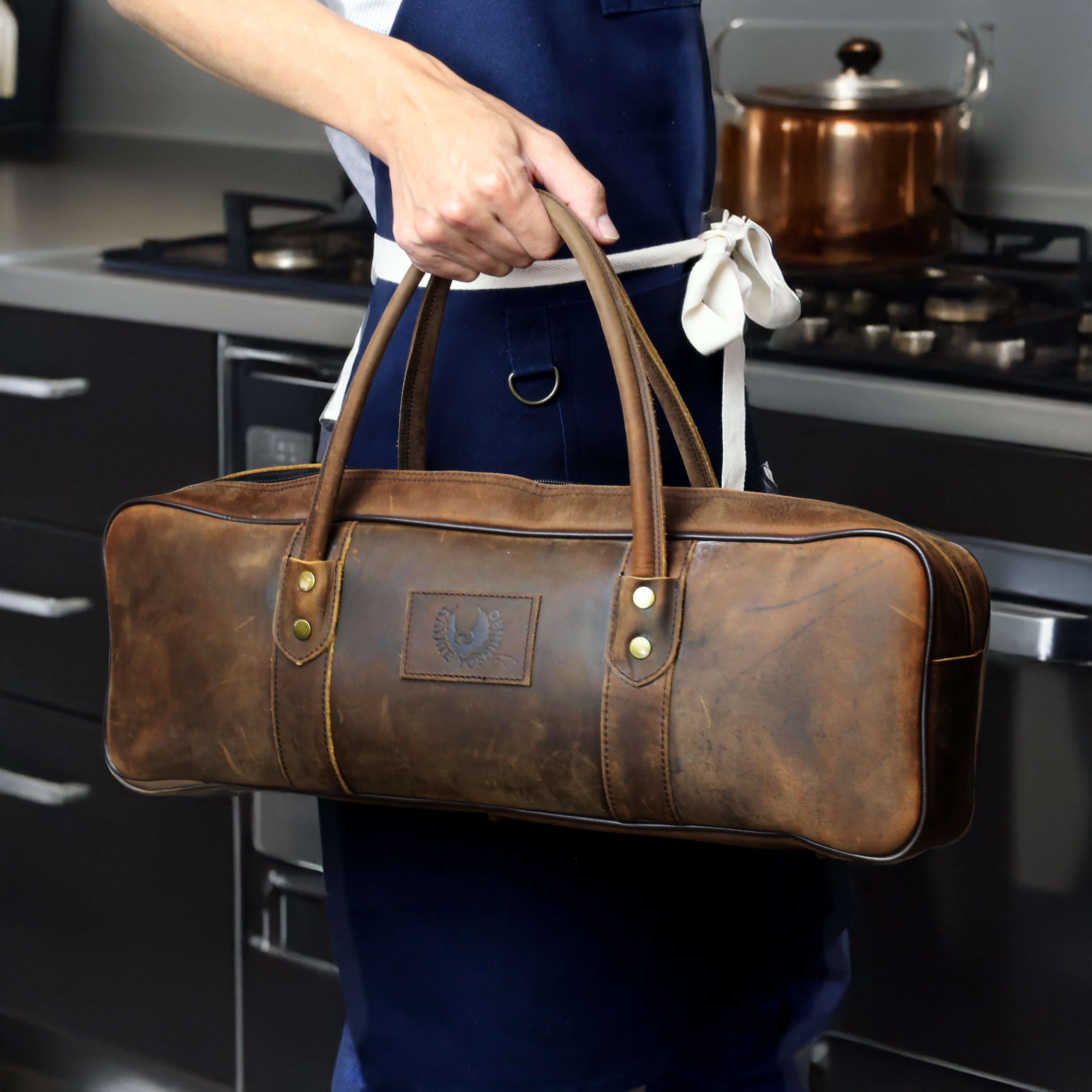 Brown natural leather knife bag carried in kitchen with front emblem and top handles