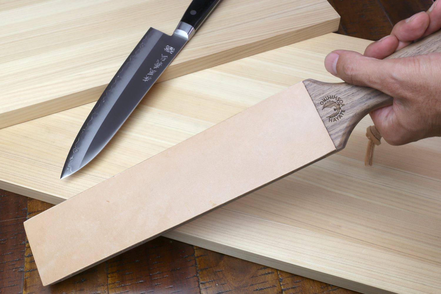 Two-sided leather strop with tan face and wooden handle, held for stropping.
