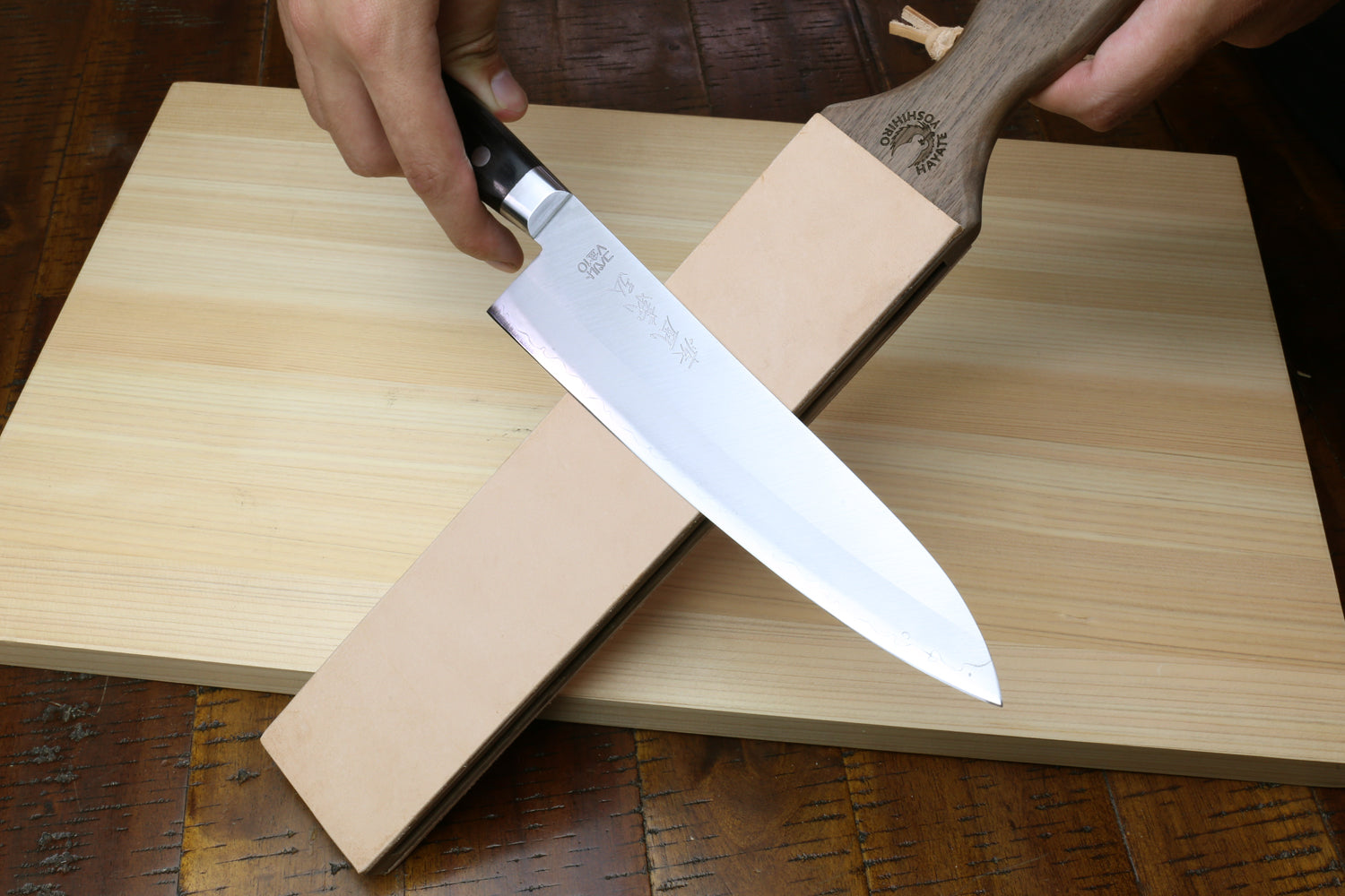 Two-sided leather strop with tan surface and wooden handle, knife resting across it.