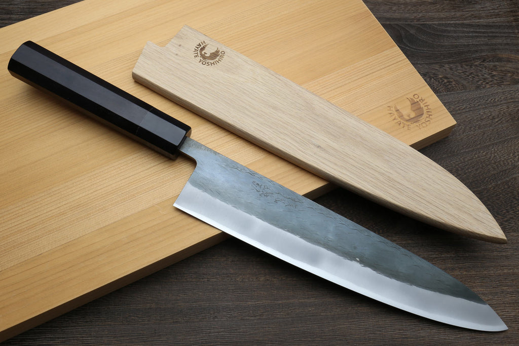 Chef's gyuto knife with black handle and blue steel blade on cutting boards