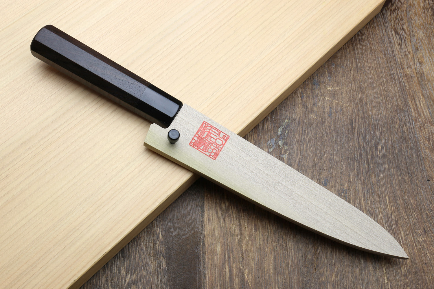 Petty utility knife with dark ebony handle and stainless blade, on light and dark boards