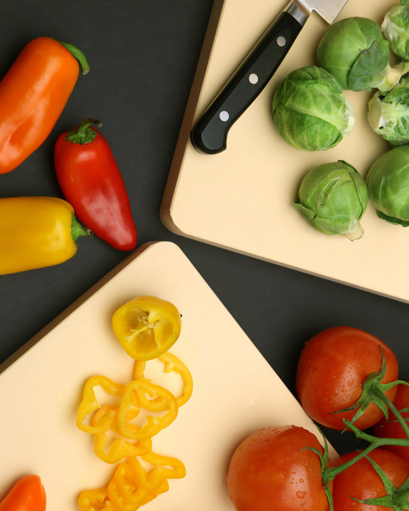 Assorted vegetables including peppers, tomatoes, and brussels sprouts on a cutting board with a knife.