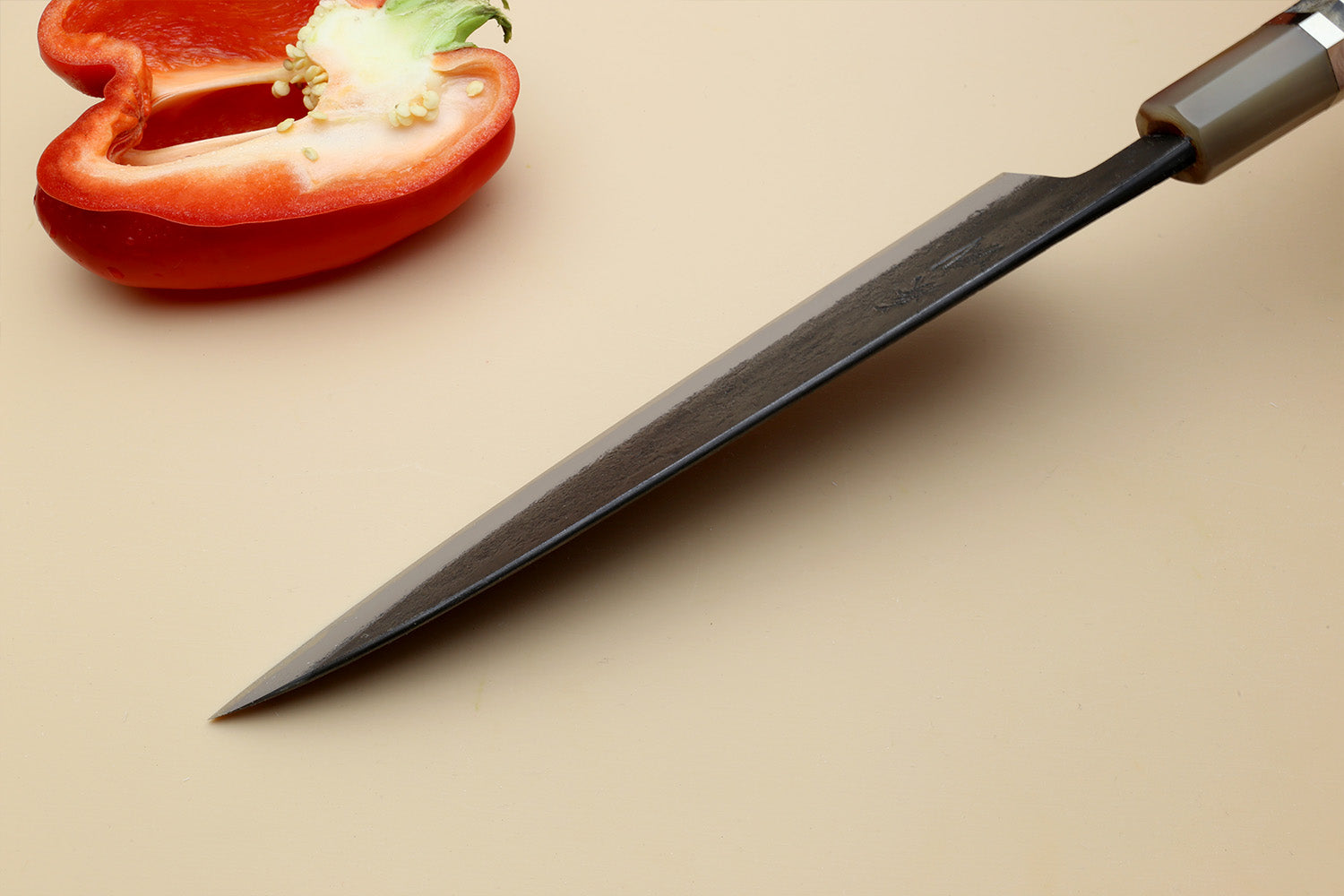 Gyuto chef’s knife tip close-up, dark blue steel blade with pointed edge.