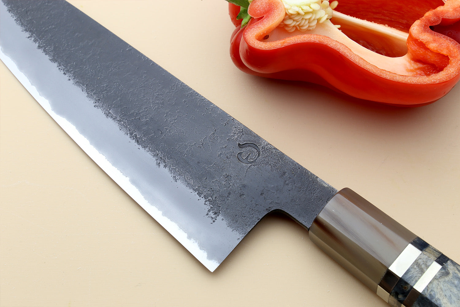 Gyuto chef’s knife blade close-up, dark blue mottled steel with etched mark near heel.