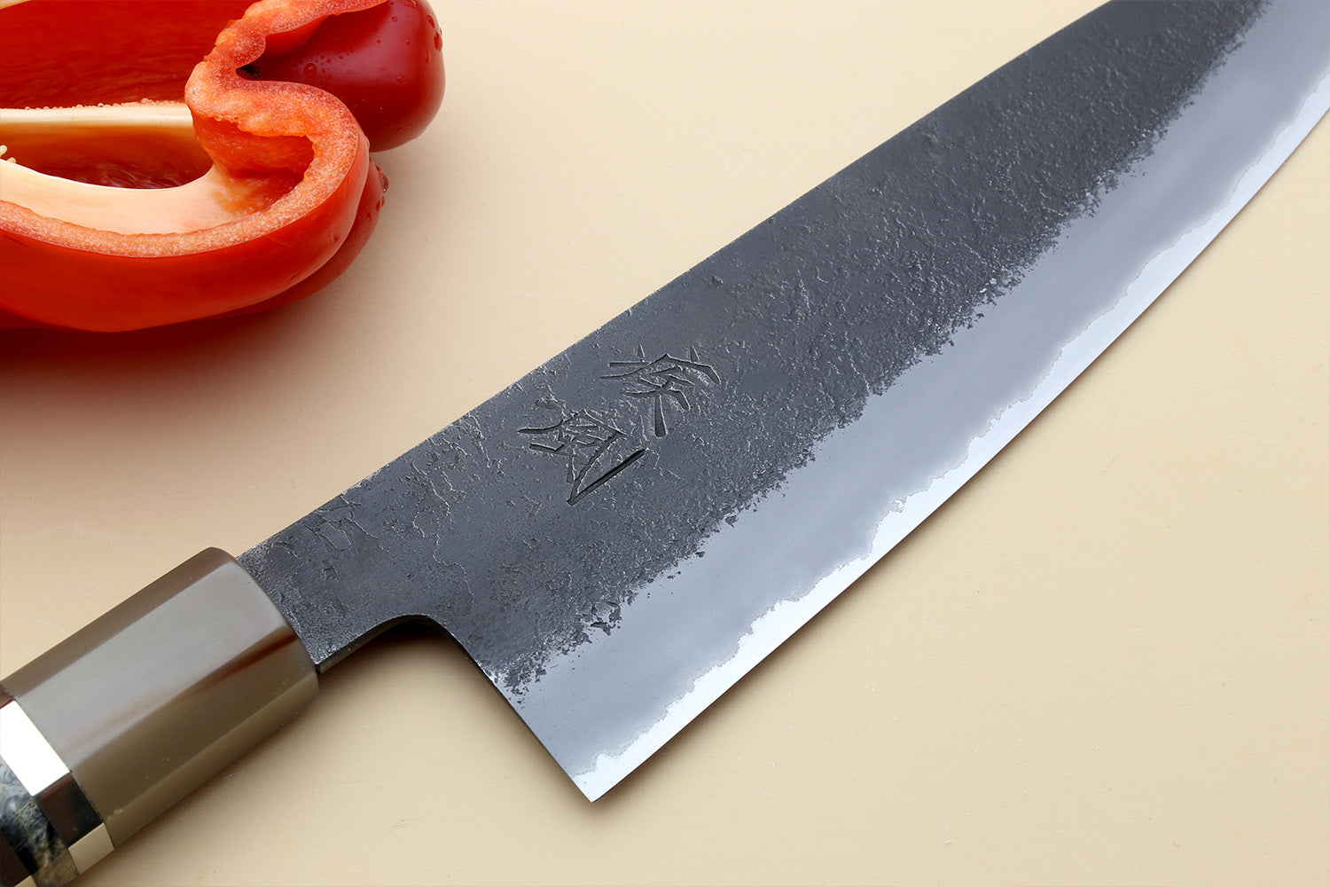 Gyuto chef’s knife blade close-up, dark blue mottled steel with etched marks.