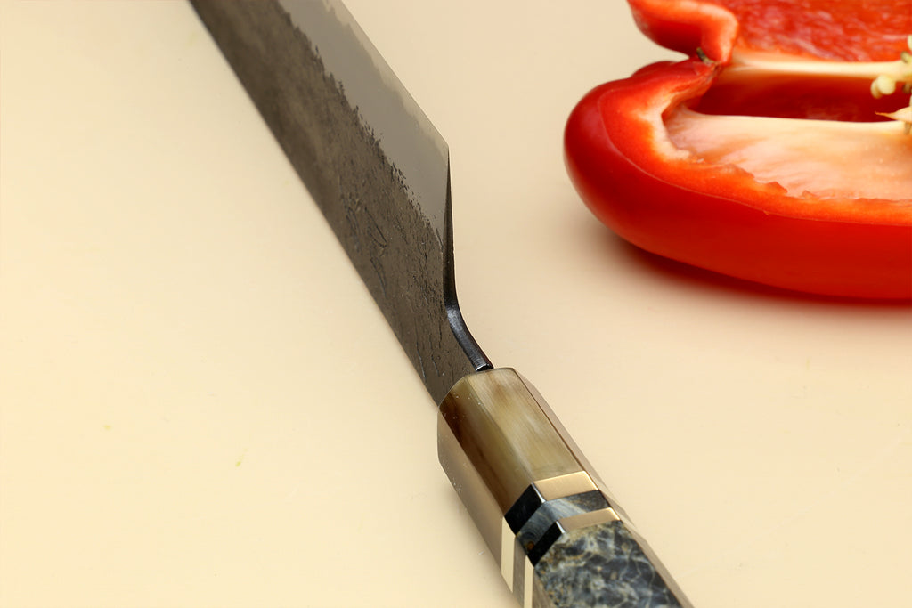 Nakiri vegetable knife blade close-up with dark forged finish and stamped markings