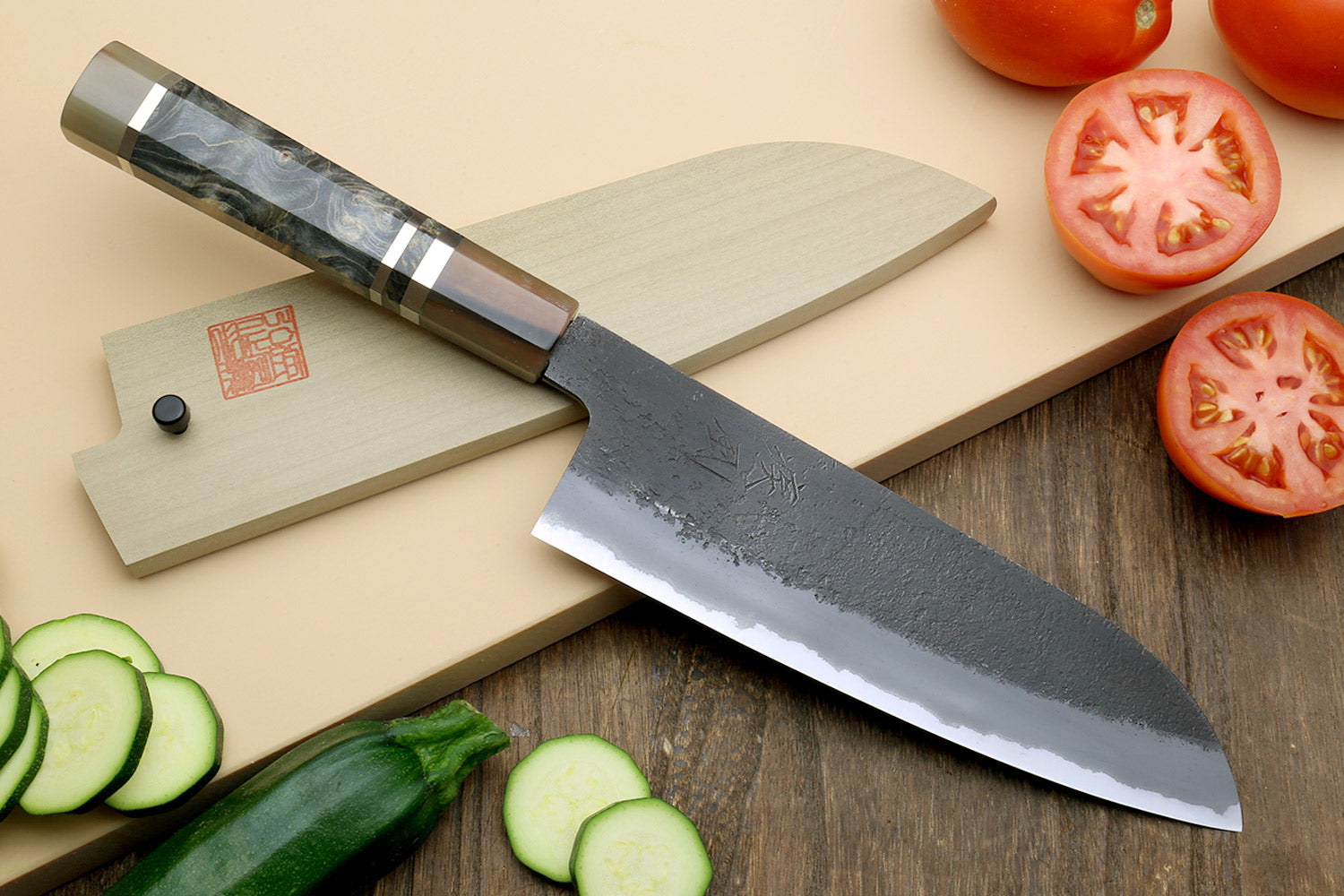 Santoku knife with blue-steel blade and dark handle, with tomato and cucumber slices