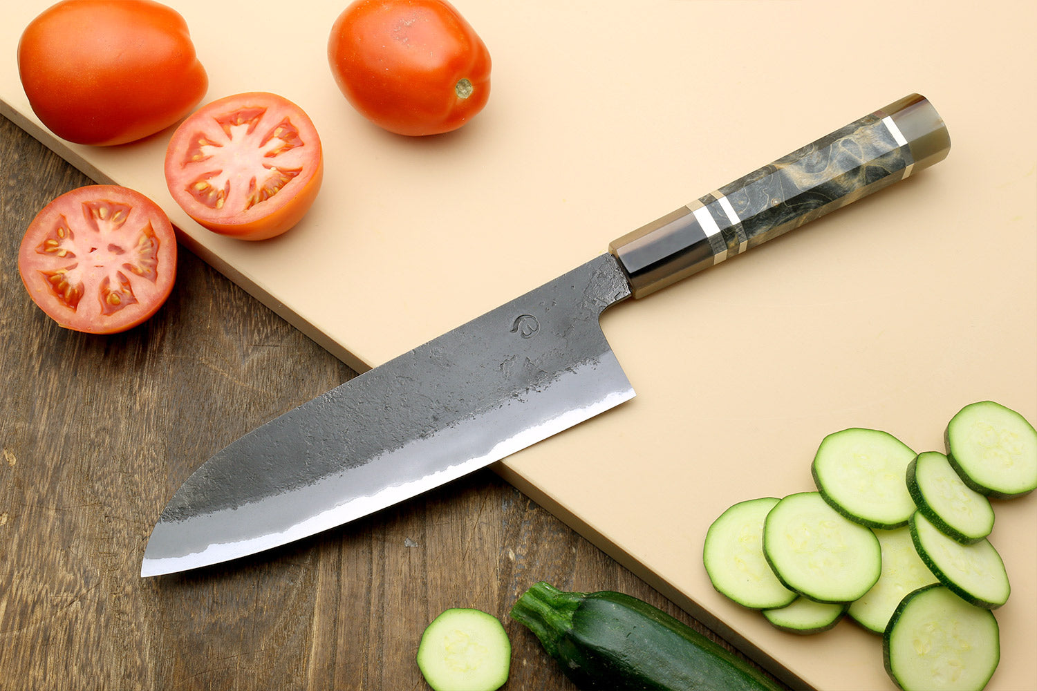 Blue-steel Santoku knife with dark handle, near sliced cucumber and tomato