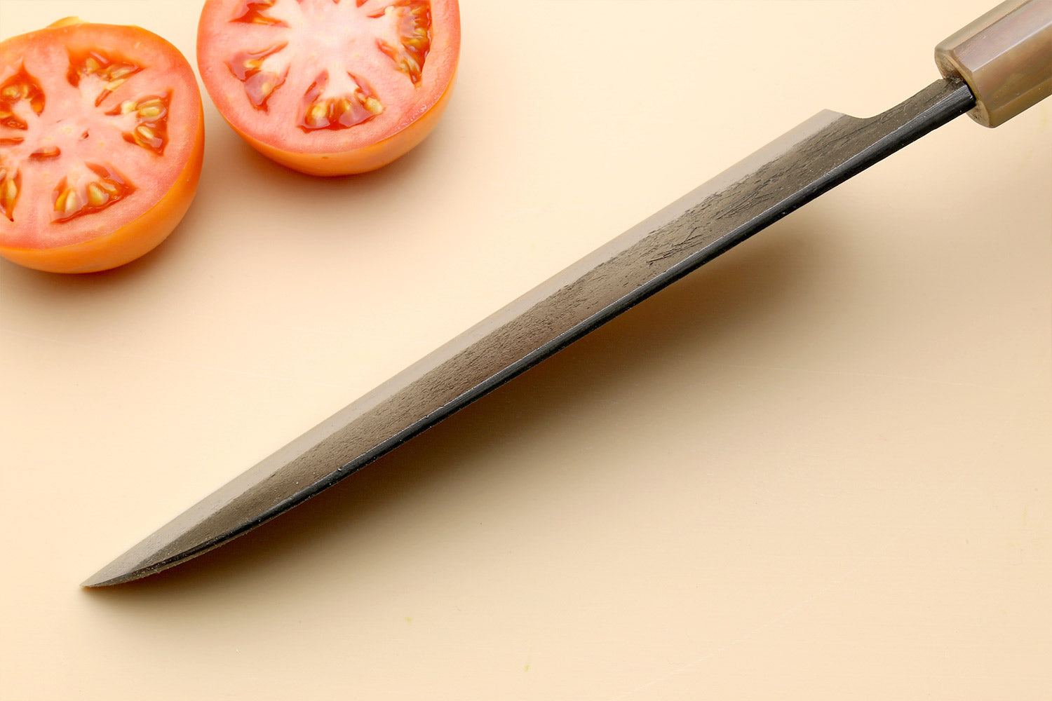 Santoku knife with blue steel blade and dark handle, angled on board