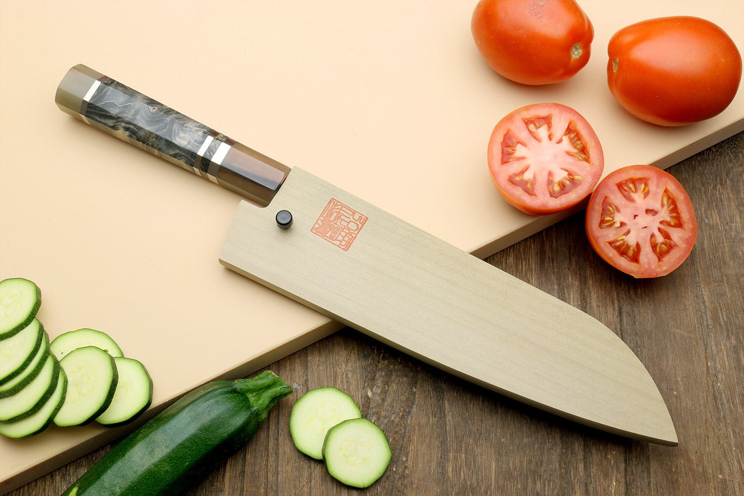 Santoku knife with blue-steel blade and dark handle, with tomato and cucumber slices