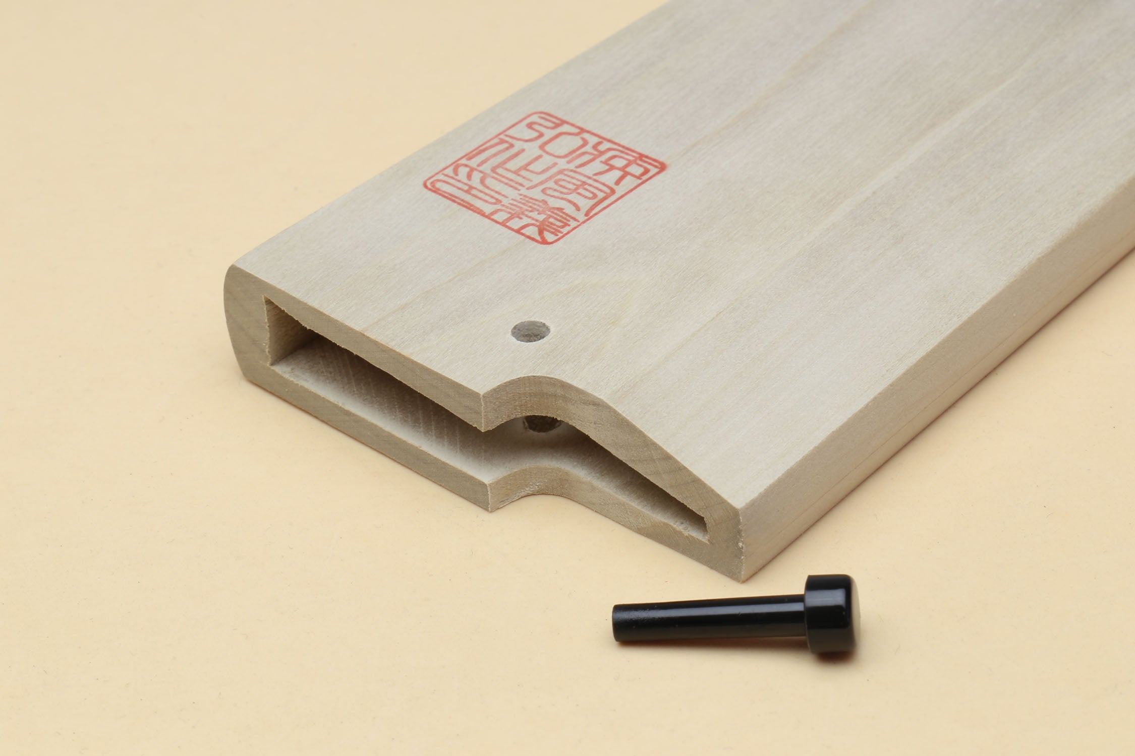 Black safety pin for deba saya cover beside a wooden saya cover slot