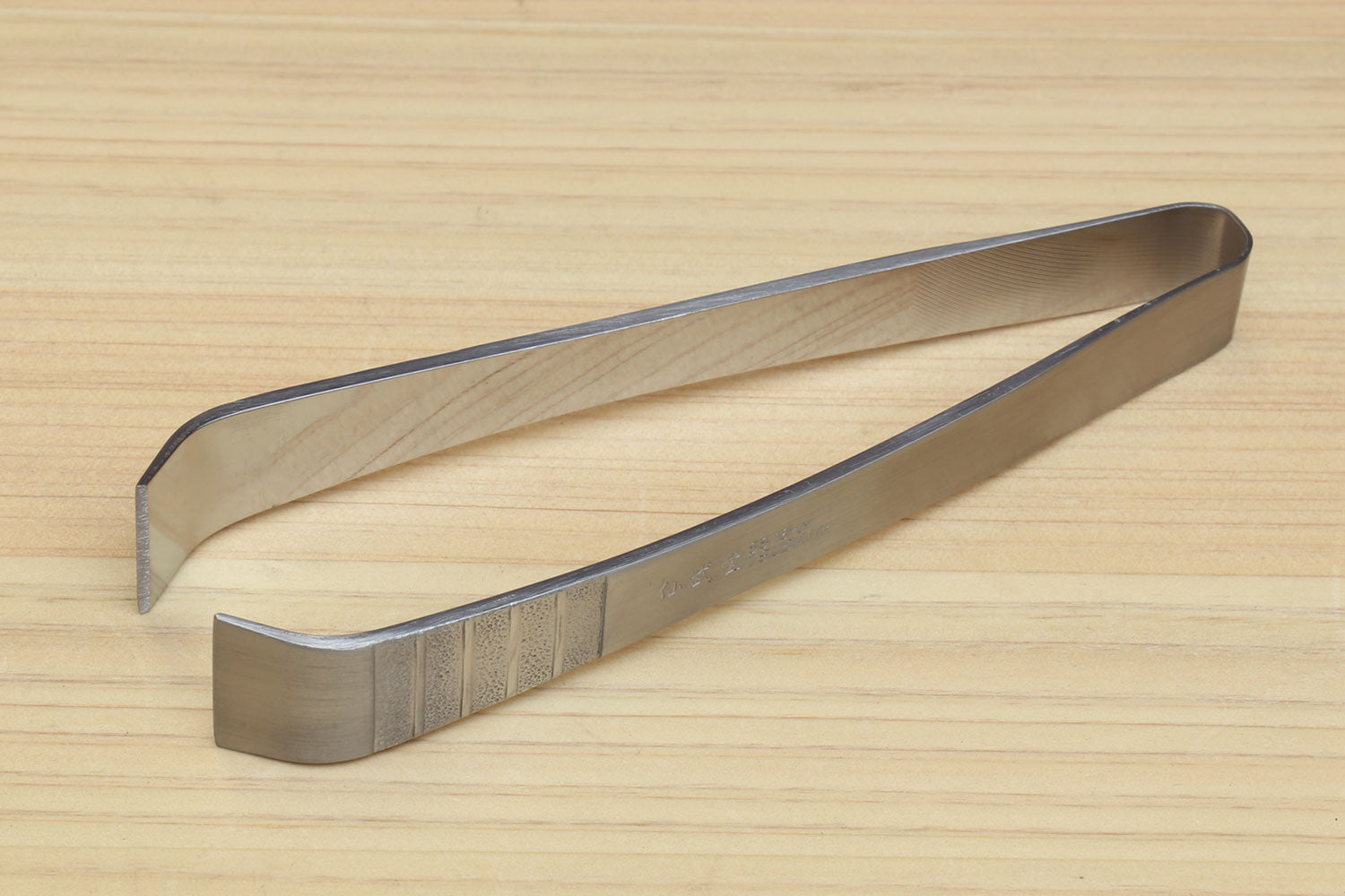 Stainless steel tweezer with extended V-shaped jaws on wooden board