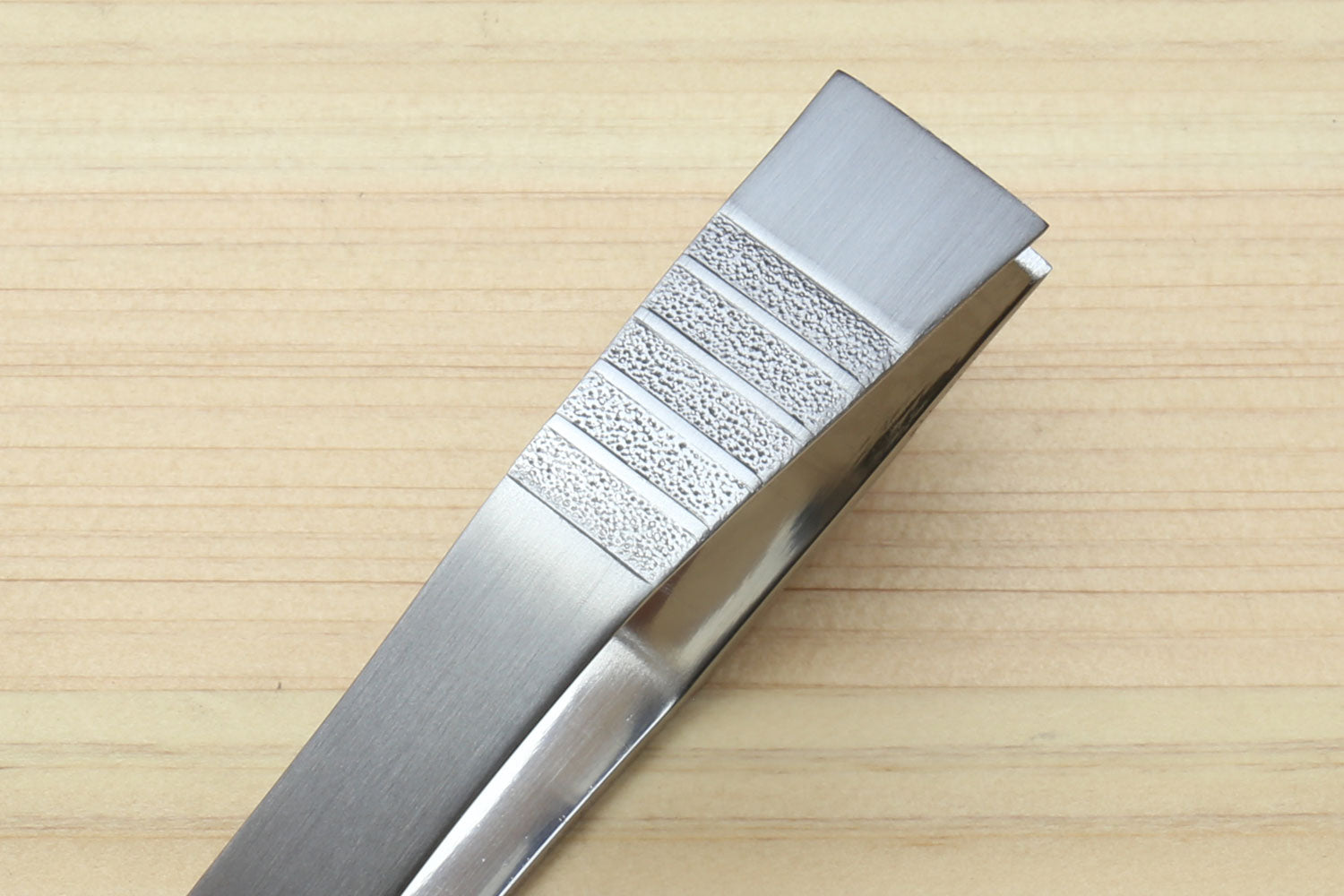 Non-slip fish bone tweezers close-up with textured grip panel on brushed metal.