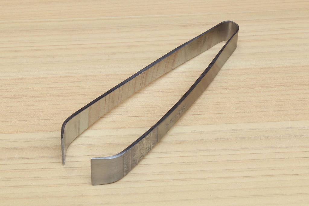 Stainless steel tweezer with V-shaped jaws on wooden board, side view