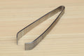 Stainless steel tweezer with V-shaped jaws on wooden board, side view