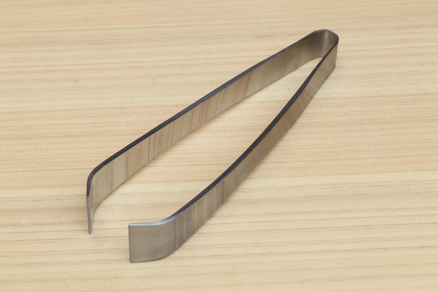 Stainless steel tweezer with V-shaped jaws on wooden board, side view