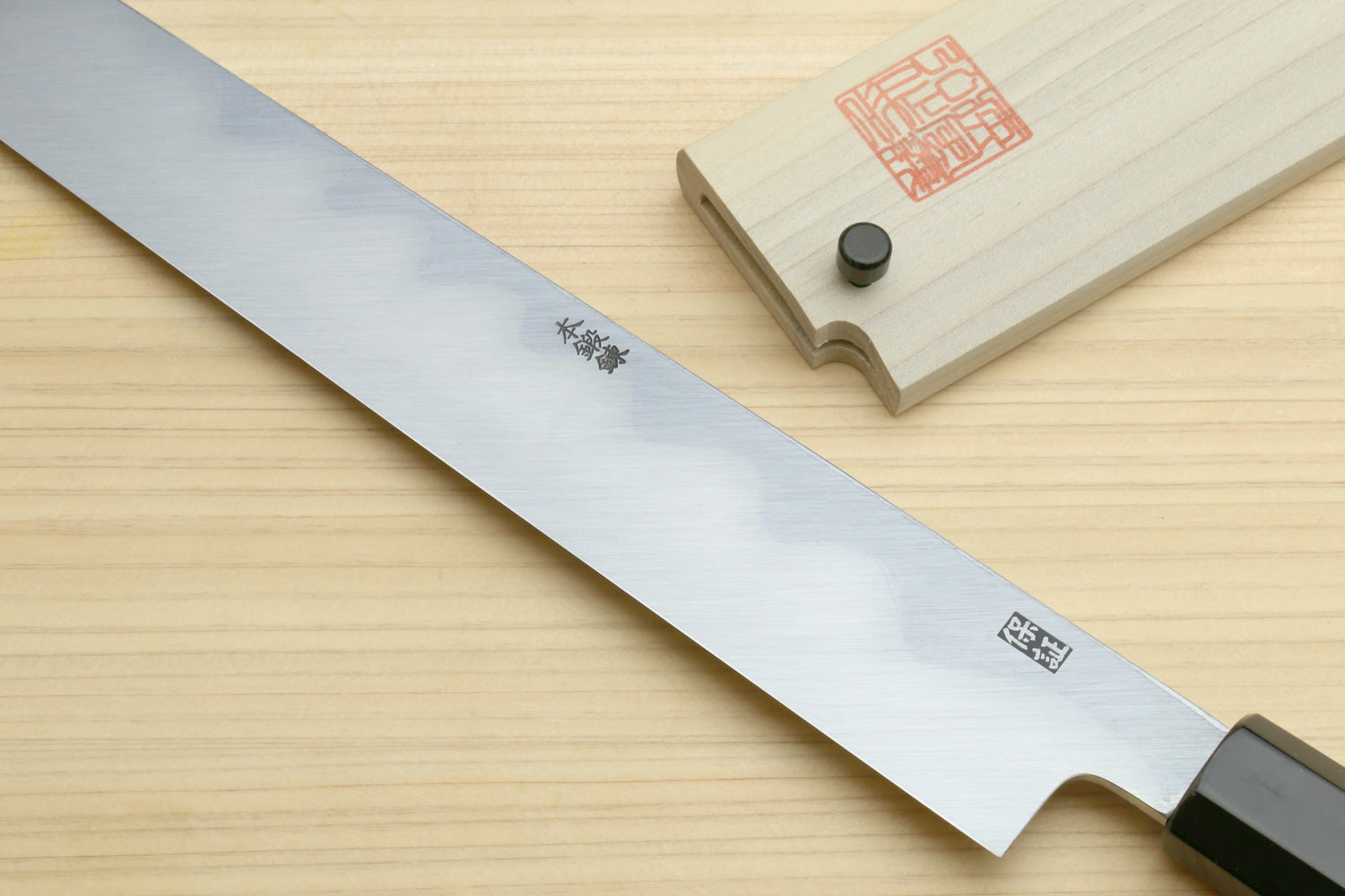 Japanese kiritsuke knife blade close-up with etched markings and black handle
