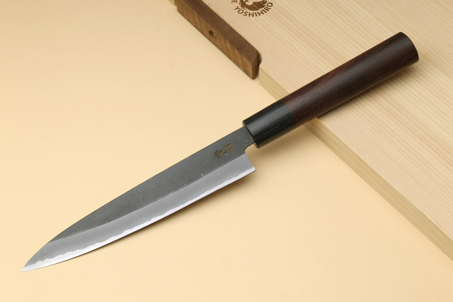 Petty knife with dark wood handle and blue steel blade on a light wooden board