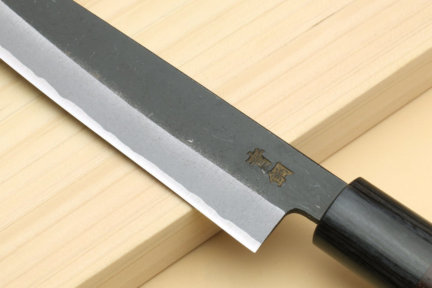 Petty knife blade close-up with engraved logo near bolster and dark wood handle