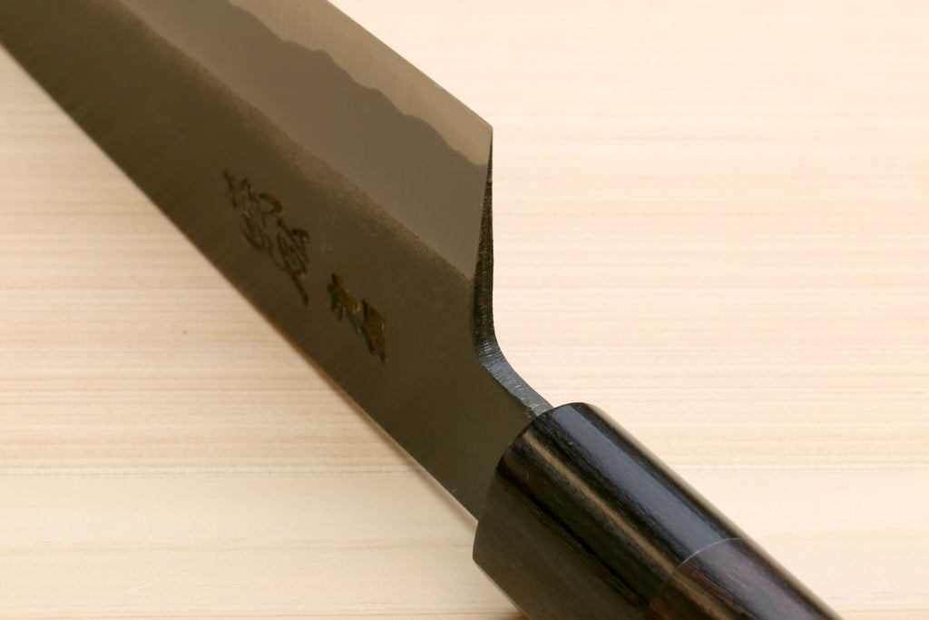 Chef knife with dark D-shaped handle and blackened blue steel blade heel close-up