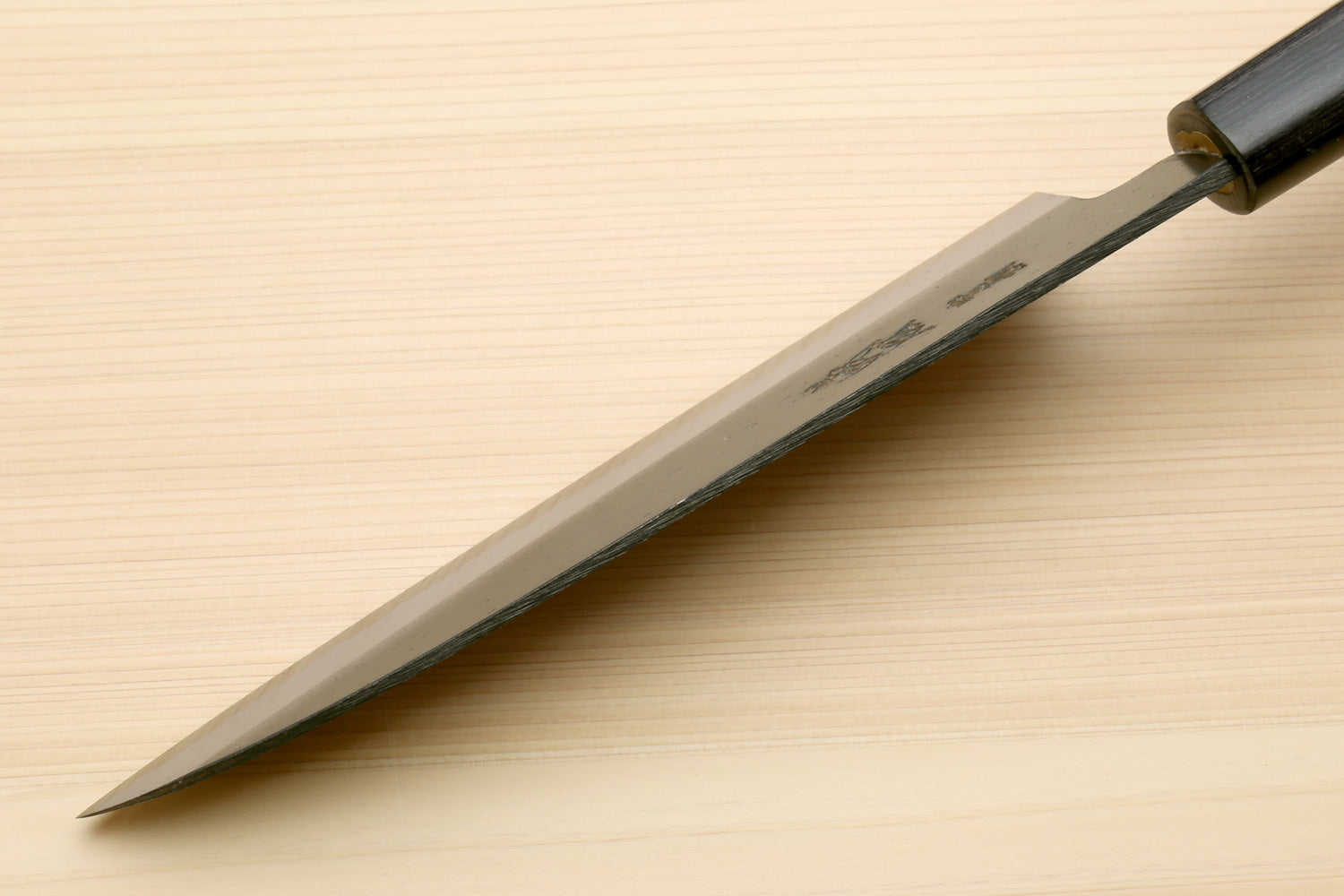 Chef knife with blackened blue steel blade and dark D-shaped handle, tip view