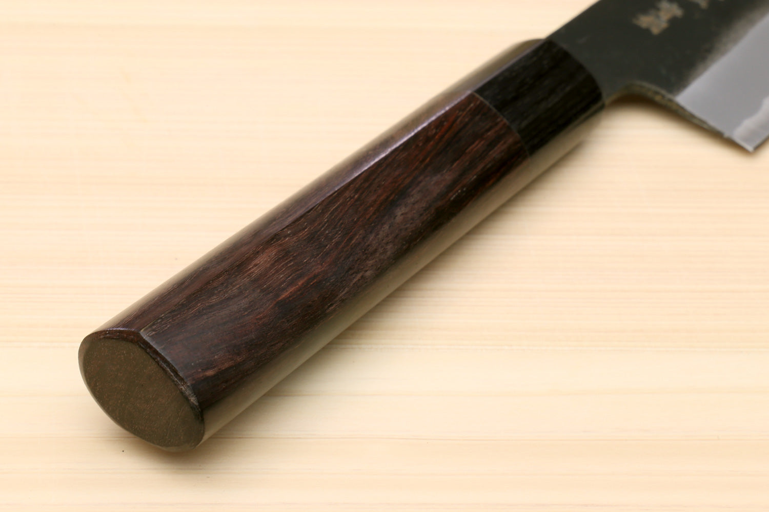Chef knife with dark D-shaped handle and blackened blue steel blade, butt end view