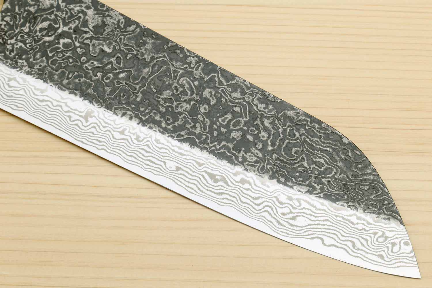 Damascus santoku blade with wavy pattern and pointed tip on light wood