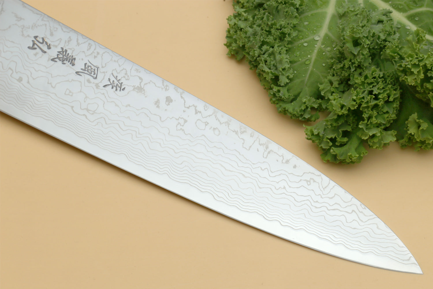 Damascus gyuto chef knife blade close-up with wavy pattern and engraved markings