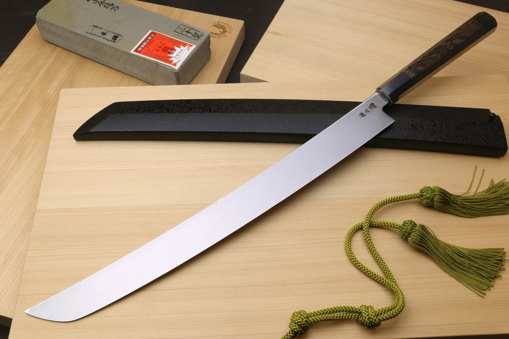 Tuna knife with long silver blade and dark handle, shown with black sheath and box