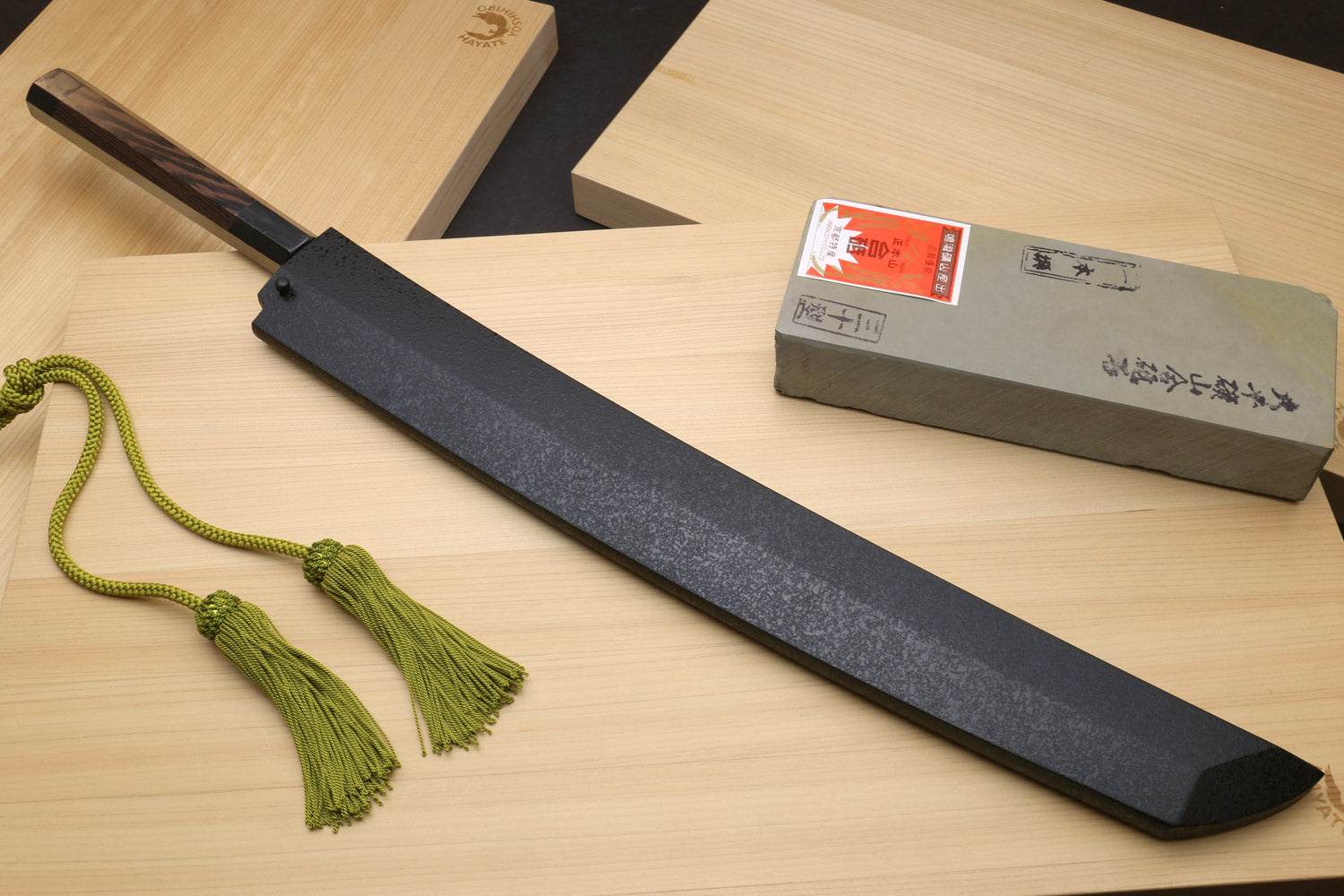Tuna knife with dark saya, long silver blade, green tassel cord, and wrapped box