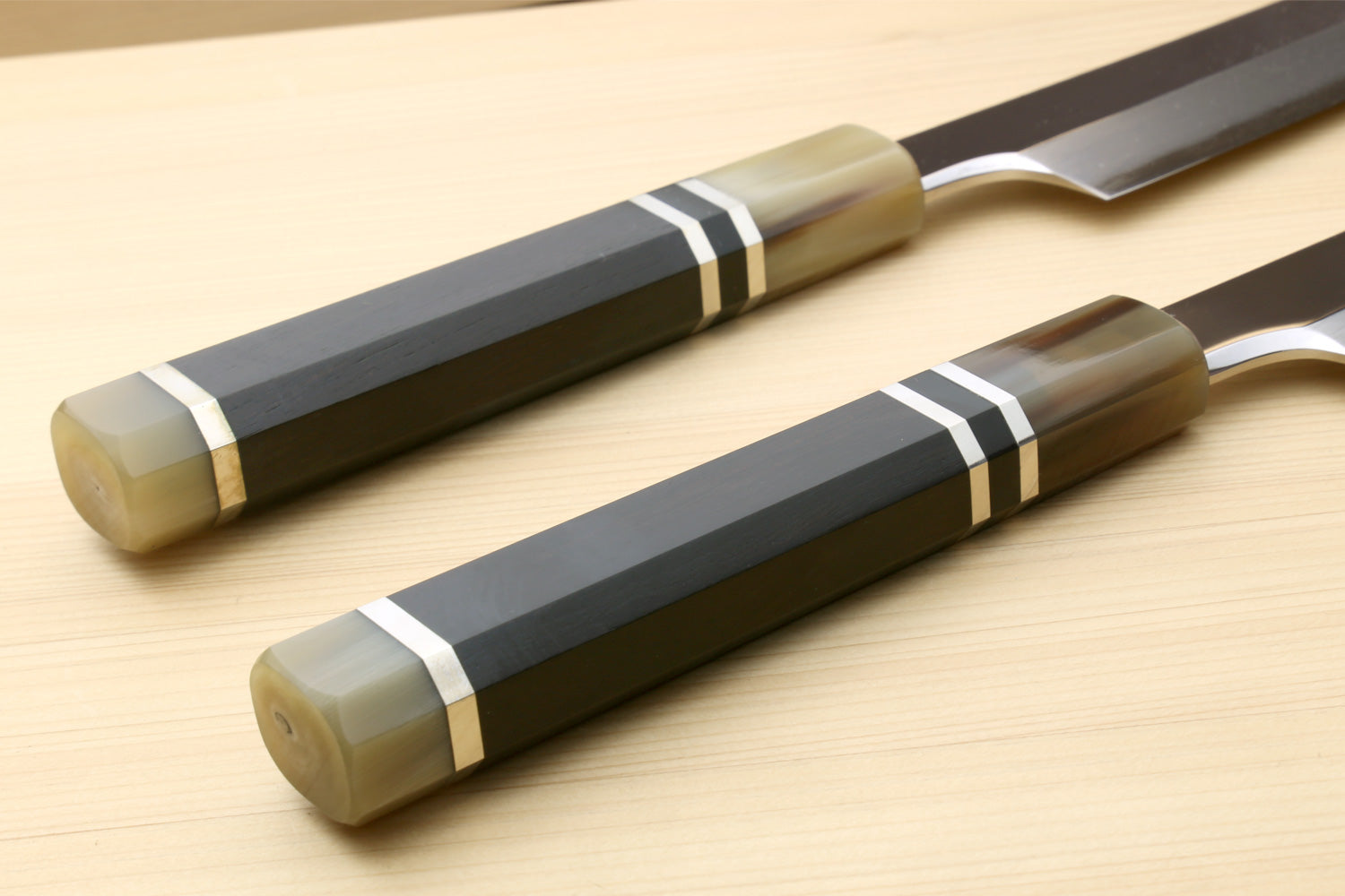 Ebony knife handles with triple-ring accents and dark sheath beside mirror stainless blade