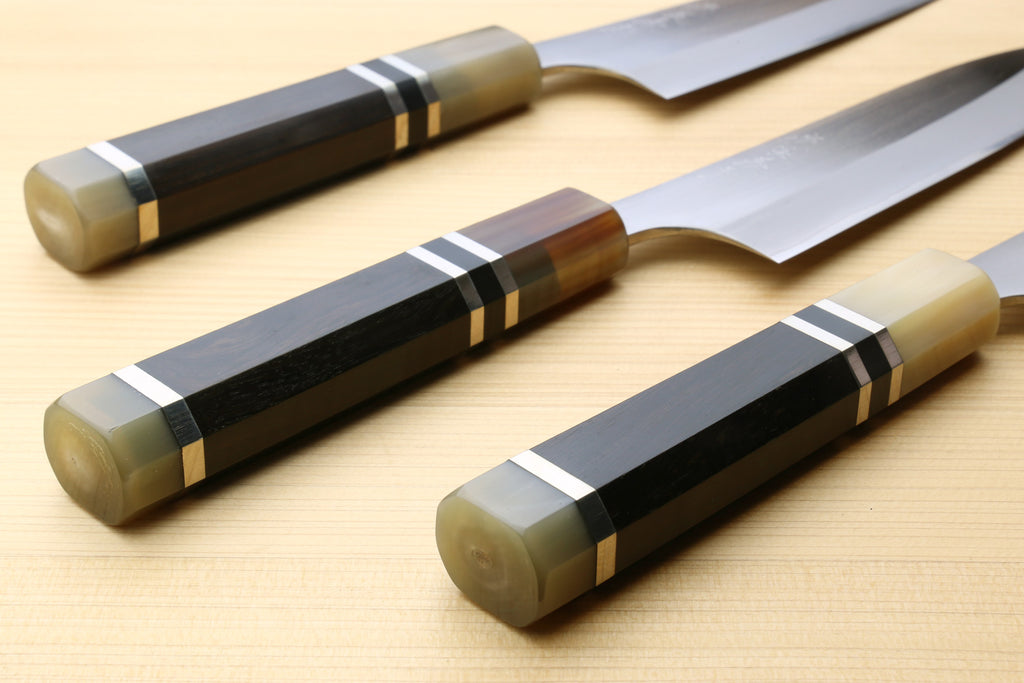 Petty utility chef knives laid on board, stainless blades and dark handle rings