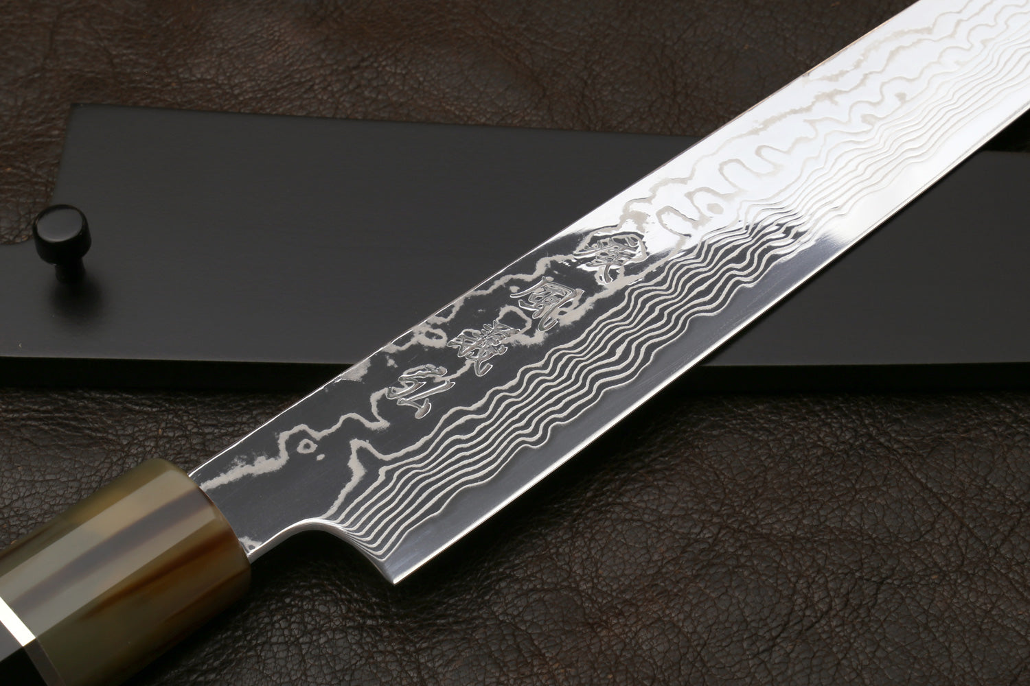Sujihiki slicer knife with close-up damascus pattern on blade and dark handle rings