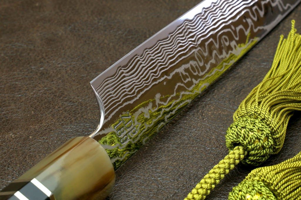 Sujihiki slicer knife blade close-up with damascus lines and gold-toned handle collar