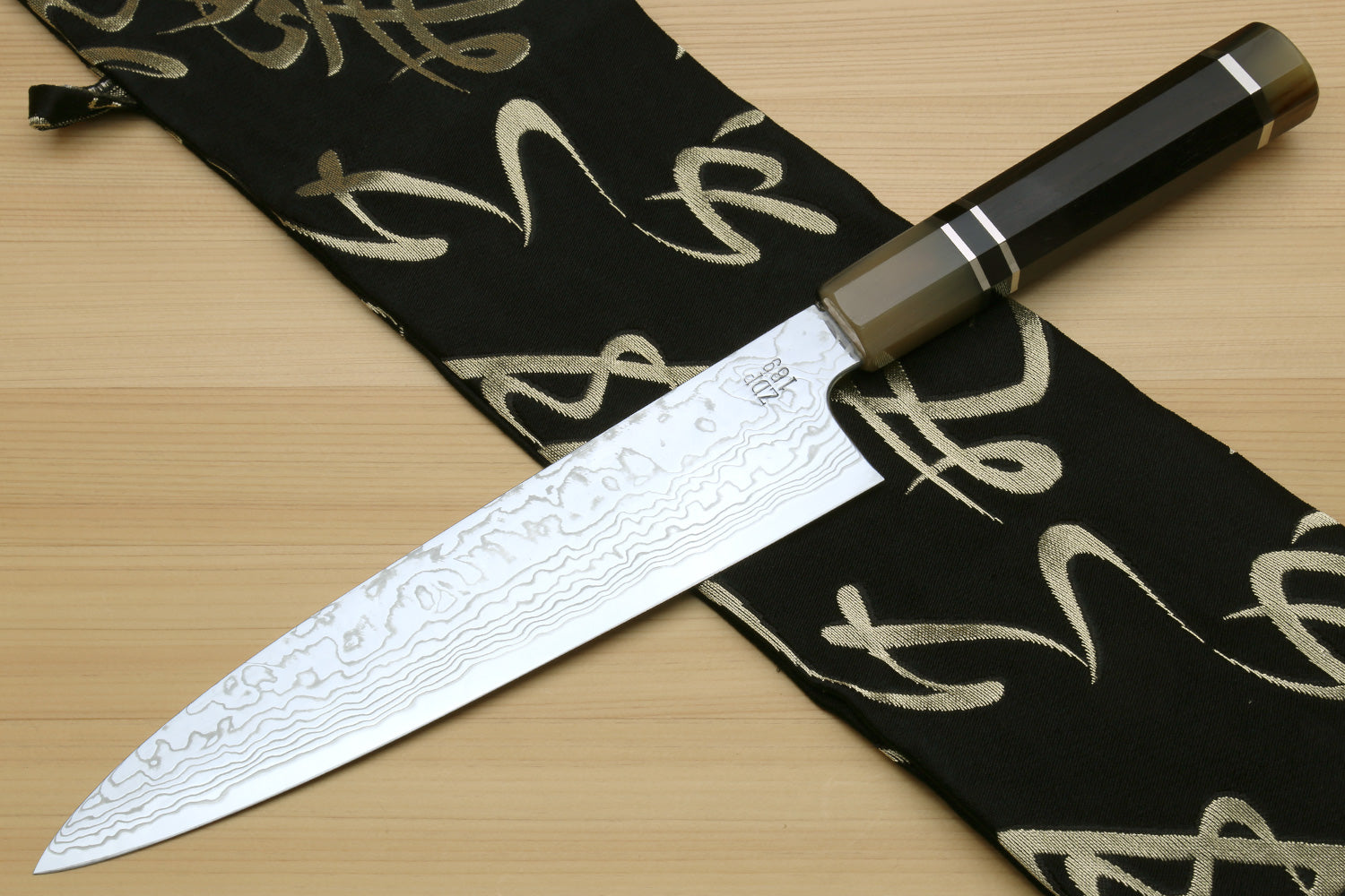 Damascus gyuto chef knife with blade and dark octagonal handle on black cloth