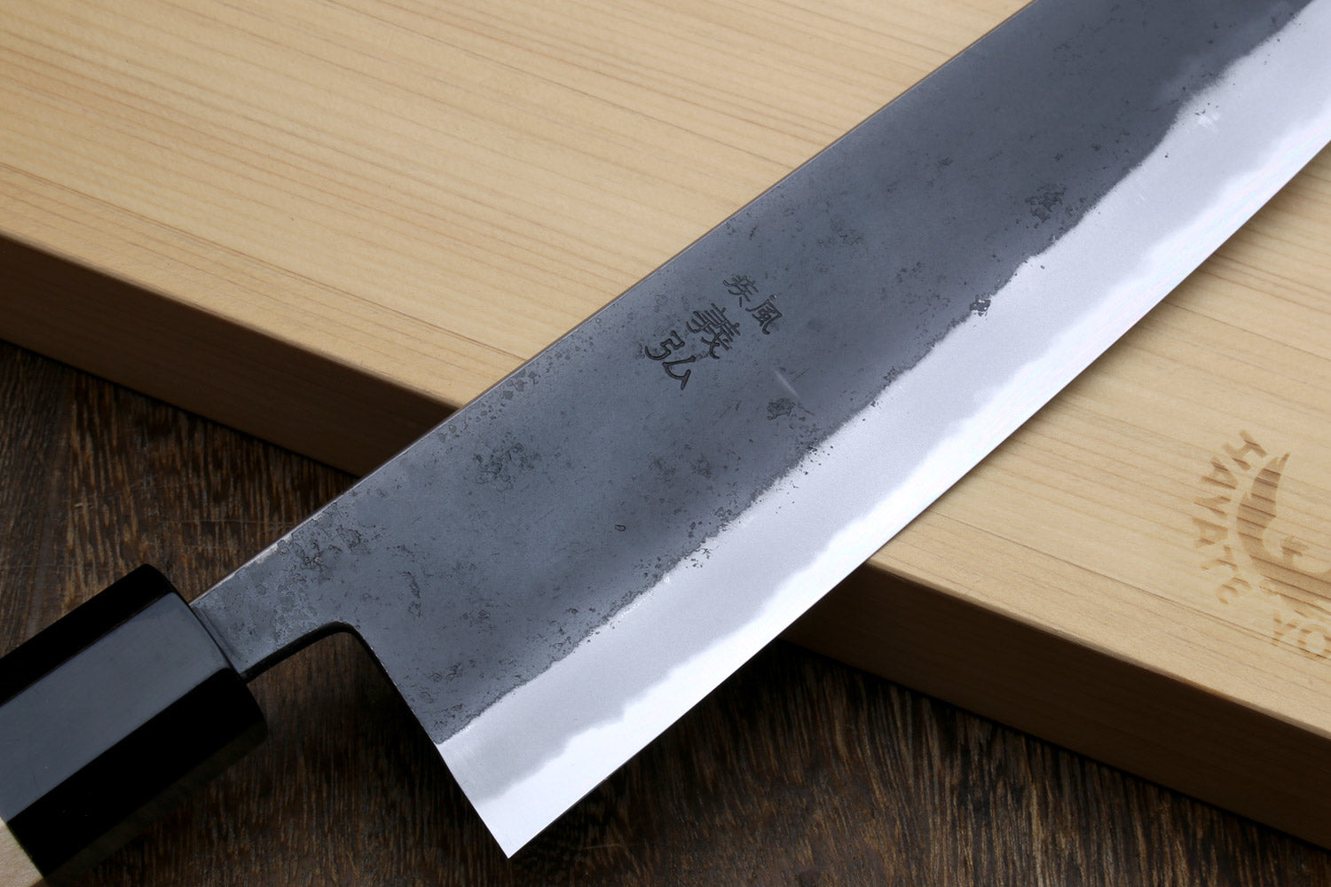 Blue steel gyuto knife blade with etched markings, kurouchi texture, black handle collar