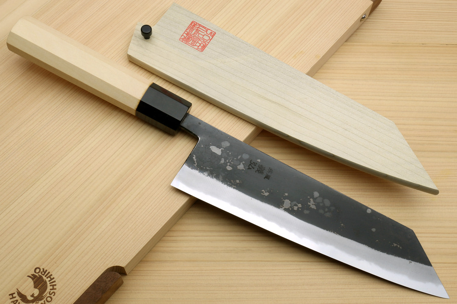 Kiritsuke chef knife with black handle, dark speckled blade, and light wood saya cover