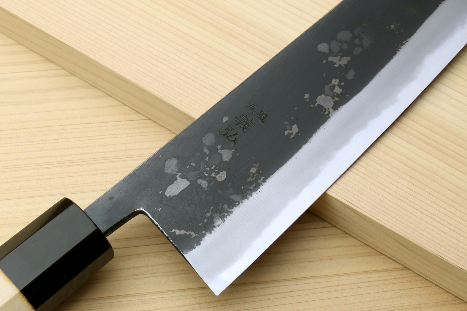 Japanese kiritsuke chef knife blade close-up with dark speckled finish and black handle